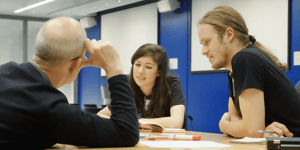 Three people sat around a table having a discussion. 