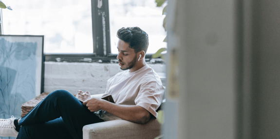 A man sat on a sofa looking down towards a notebook he's holding. 