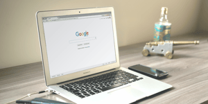 A laptop on a table with a screen showing the Google search page. 