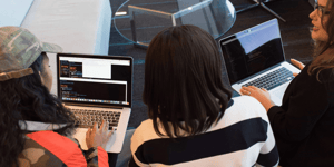 Photo of three women working on their laptops next to each other on a sofa. 