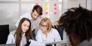 A group of marketers, two women and one man, looking at a piece of paper, brainstorming ideas together.