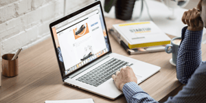 A man looking at a website on a laptop with his hand resting on the mouse trackpad.