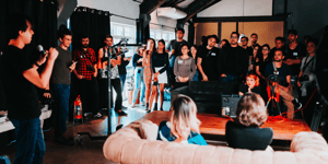A speaker talking in front of a crowd standing in a room. 
