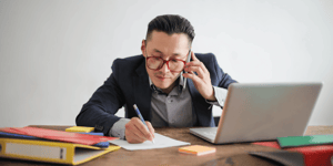 A salesman on talking to someone on the phone and writing notes down on a piece of paper. 