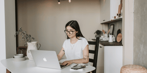 A woman working at home sat on her desk looking at her laptop. 