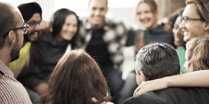 A group of people in an improv class huddled together in a circle with arms around each other's shoulders. 