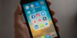 Hand holding an iPhone showing a screen of social media apps.