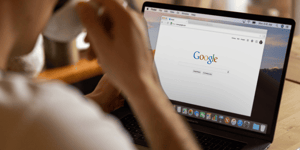 Person drinking a cup of coffee and looking at Google on a laptop screen. 