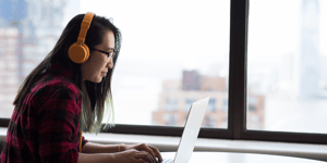 A woman wearing headphones working on her laptop in an office.