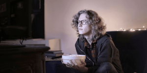 A man watching the TV with a bowl of popcorn in his hand.