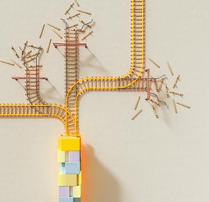 A conceptual image featuring a set of train tracks branching in multiple directions, with some sections incomplete or broken. The tracks emerge from a colourful stack of blocks at the bottom, symbolising a foundation or starting point. The scattered and disorganised tracks illustrate the challenges of having no clear strategy or direction.